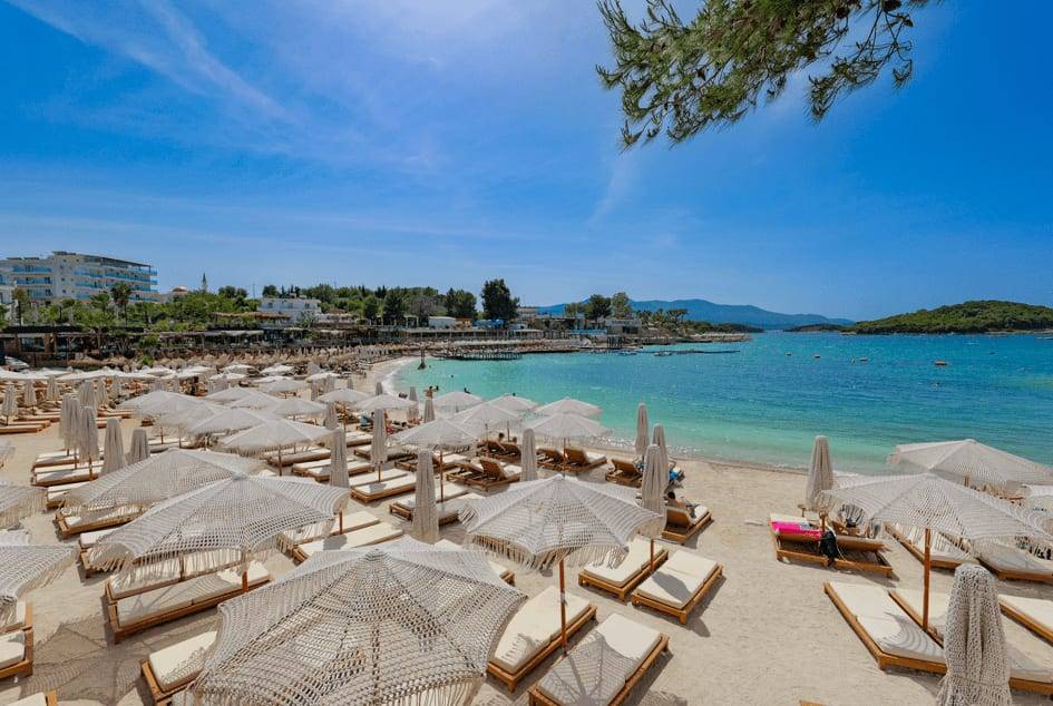 Greg Beach in Ksamil: rows of sunbeds under macramé parasols beside the turquoise water