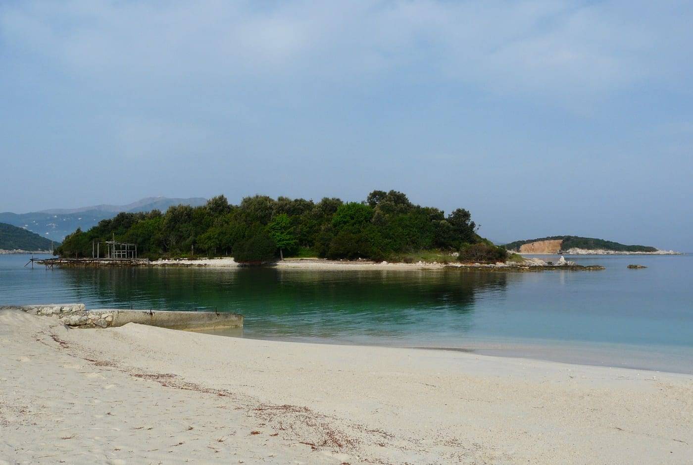 One of the wooded islets of Ksamil across calm water from a white-sand beach