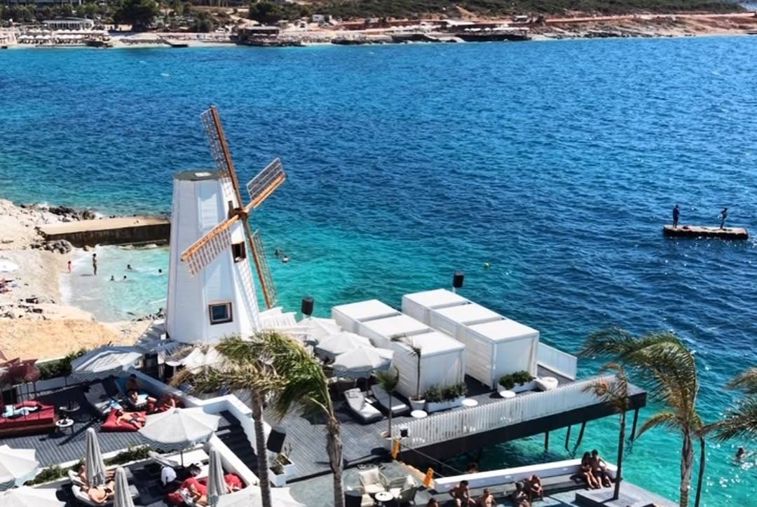 Mulino Beach in Ksamil from above: the white windmill, cabanas over the water and the pool
