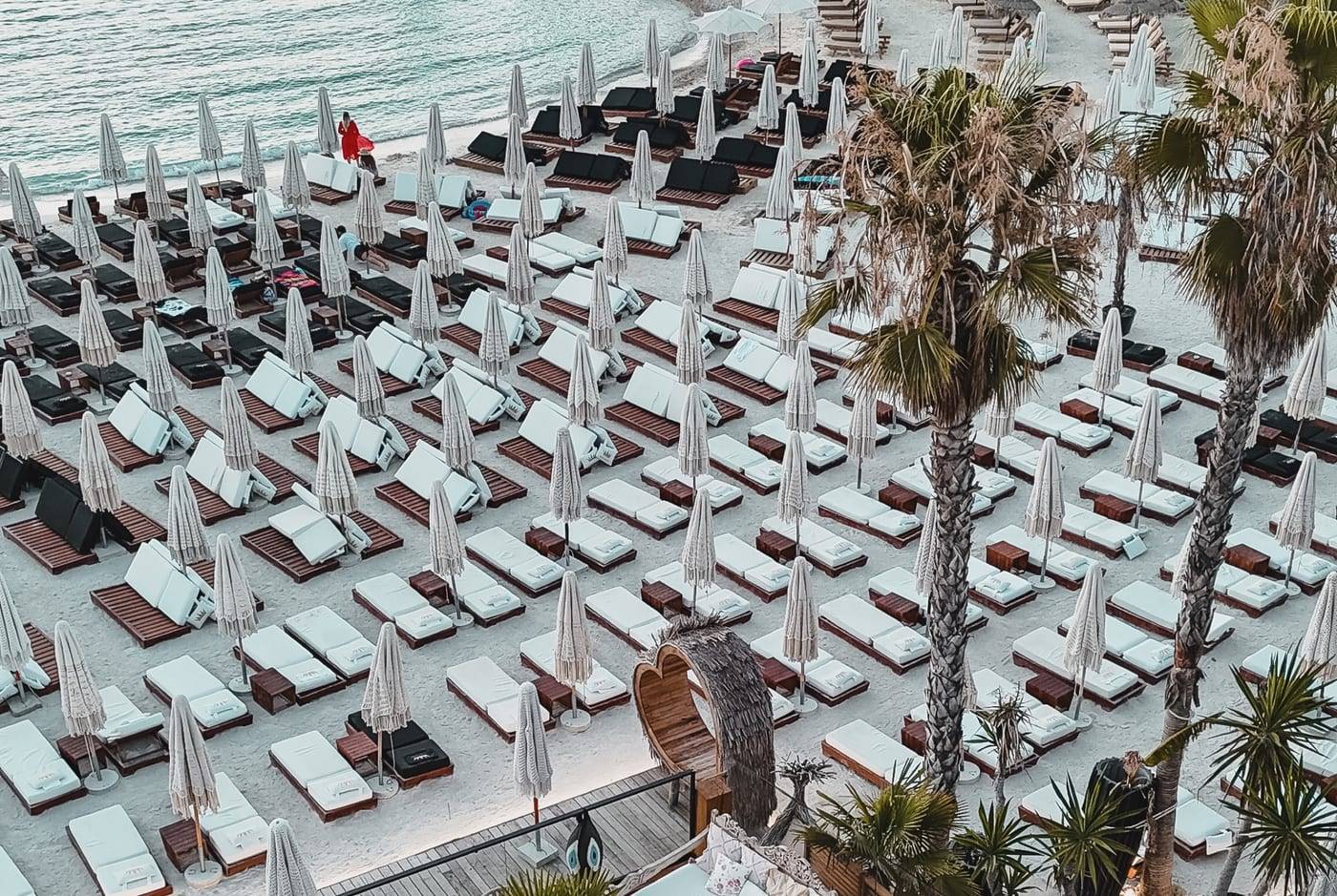 Principotes in Ksamil from the air: rows of white sunbeds and parasols between palm trees and the sea
