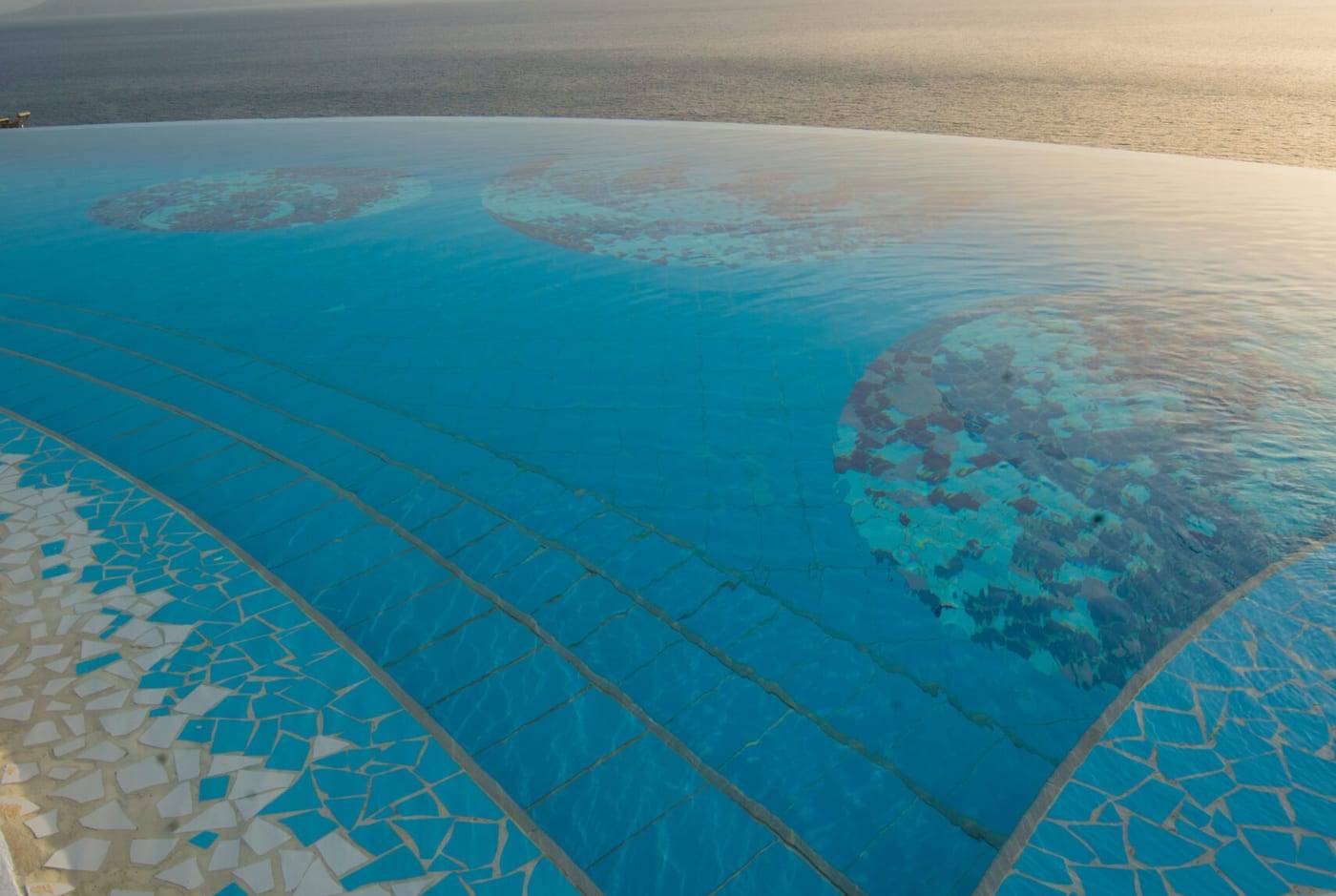 Le bord de la piscine à débordement du Bougainville Bay Resort & SPA dans la lumière douce du coucher de soleil, avec la mer derrière