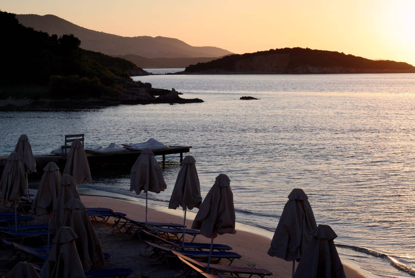 Sunset over the islets of Ksamil, with closed beach parasols on the shore