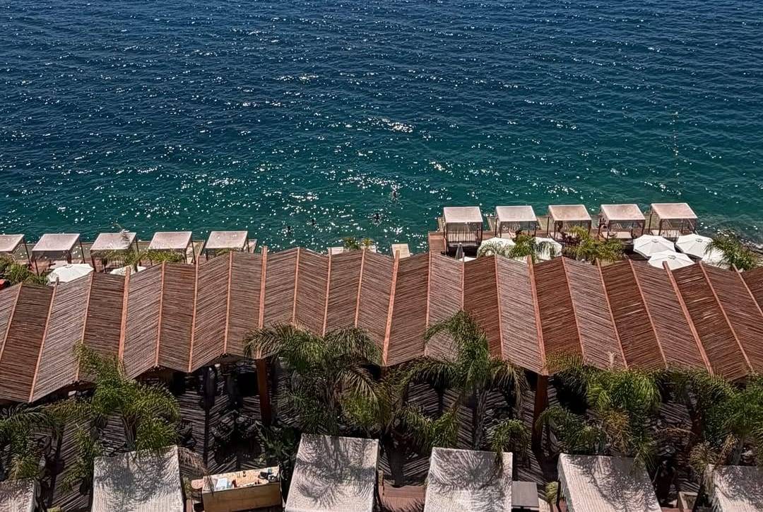 Lost Seaside on the coast road south of Saranda, from the air: cabanas with wooden roofs, palm trees and the sea