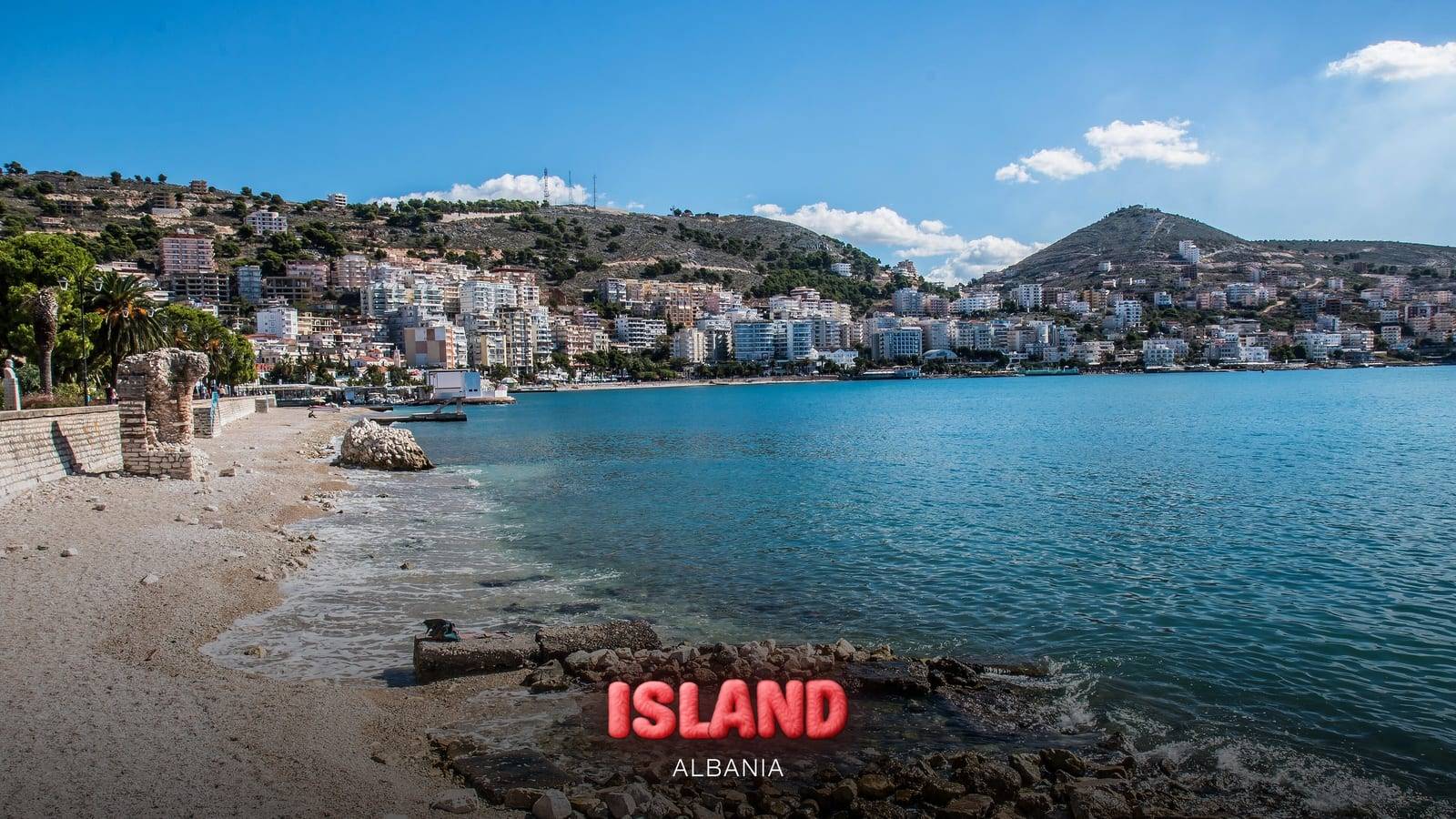 The beach and bay of Saranda with the town and the hills behind, Albania, with the Party Island Albania logo